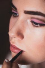 Naklejka premium The work of a professional makeup artist. Hand of make-up master, painting lips of young beautiful model.