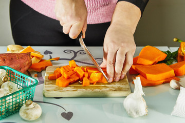 Woman slices a pumpkin on a wooden board in the kitchen. Female hands prepare cream soup with pumpkin. Healthy eating concept.