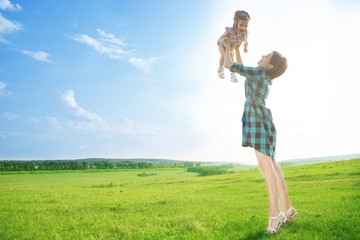 A beautiful mother with a cute daughter is playin on green field