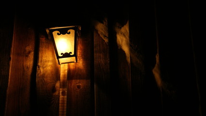 warm light of a lantern on a wooden wall of an alpine hut in the night