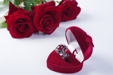 Signet with a stone in a gift box, two red hearts and a bouquet of red roses. On a white background.