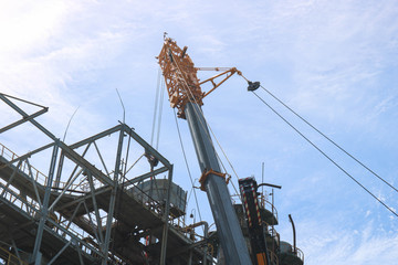 Construction and installation work with a powerful construction crane of a large new industrial oil refining petrochemical chemical plant with pipes, columns, railings, stairs and equipment
