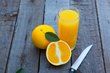 Orange juice in glass with orange, cut with a knife laying on the side on wooden table.