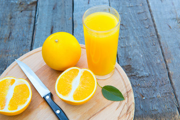 Orange juice in glass with orange, cut with a knife laying on the side on wooden table.