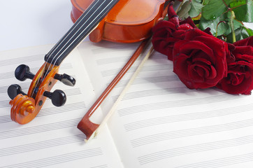 Fototapeta premium Violin with a bow, a bouquet of red roses and clean sheet music.
