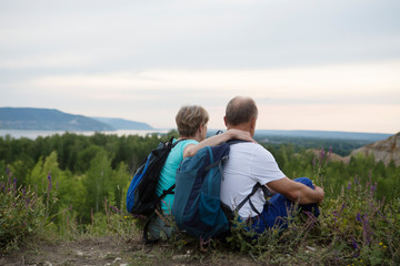 Fototapeta na wymiar Quality Time. elderly couple with backpacks sits on the mountain. Senior couple walking in nature. Outdoor activities on weekends. St. Valentine's Day