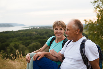 Quality Time. elderly couple with backpacks sits on the mountain. Senior couple walking in nature. Outdoor activities on weekends. St. Valentine's Day