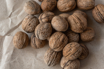 A handful of inshell walnuts on old crumpled kraft paper, brown background, warm beige picture, Top view, copyspace