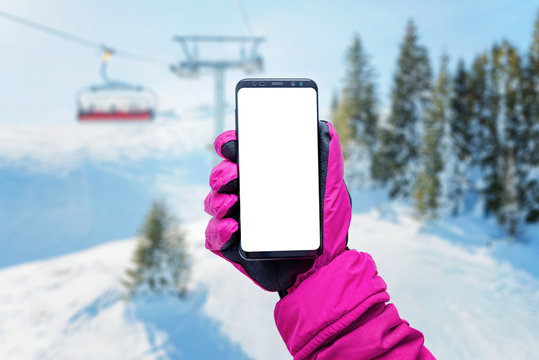 Phone in girl hand with glove on a ski lift. Isolated screen for mockup. Ski lift, resort and slopes in background