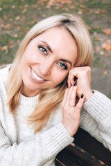 Portrait of a young woman in white sweater on the autumn leaves background.