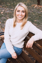 Obraz premium Portrait of a young woman in white sweater on the autumn leaves background.