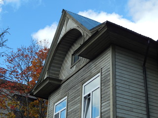 Fragment of an old wooden house with a roof and windows and near trees