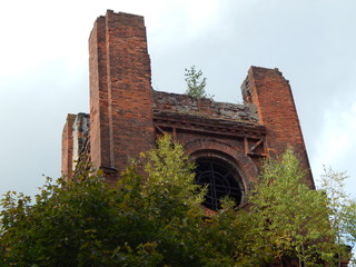 The ruins of a beautiful old architectural building made of red brick with the heroes grown on them against the sky - walls and towers