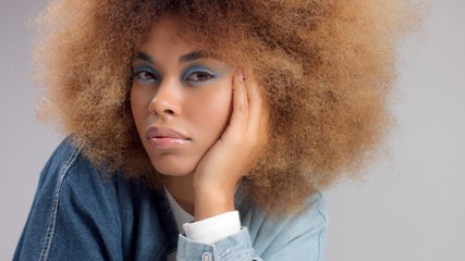closeup of mixed race black woman in denim oversized shirt and huge afro hair watching to the camera with light blue eye makeup. Z generation - 314655516