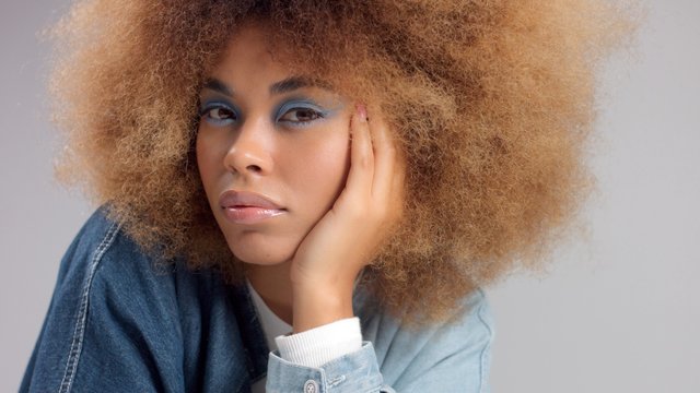 Closeup Of Mixed Race Black Woman In Denim Oversized Shirt And Huge Afro Hair Watching To The Camera With Light Blue Eye Makeup. Z Generation