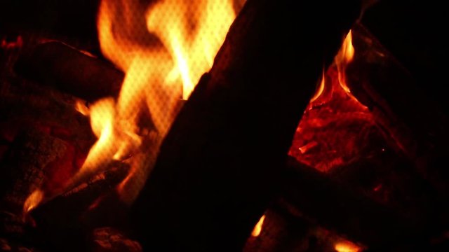 Flames burn through firewood in an outdoor fire pit at night