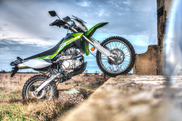 Fototapeta na wymiar Beautiful green off-road motorcycle Enduro or cross, bounced on the plate, standing on the back wheel HDR