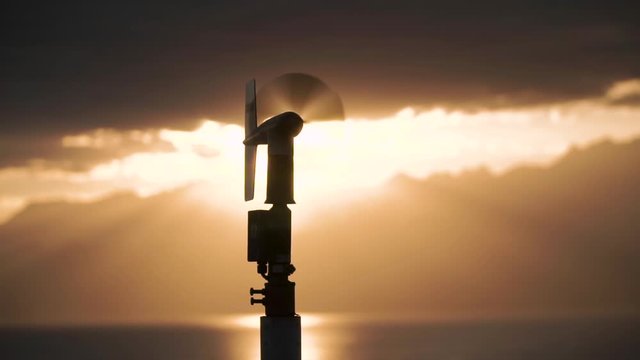 Weather vane silhouetted by the sunlight. Sunset on the lake behind the mountains