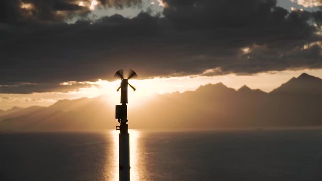 Weather vane silhouetted by the sunlight. Sunset on the lake behind the mountains