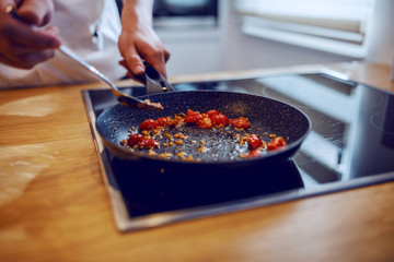 Cropped picture of creative caucasian chef in uniform standing in kitchen and preparing tomato sauce on stove.