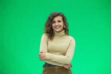 Portrait of a beautiful friendly african american woman with curly hairstyle and lovely smile isolated on a green background, her hands folded.