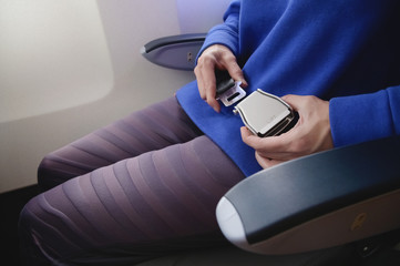 Close-up of a young woman fastens a seat belt while sitting in a passenger airplane chair by the window. The concept of safety measures for passenger flights in aircraft