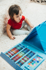 A little girl in a red t-shirt is drawing with a red marker on a blue easel