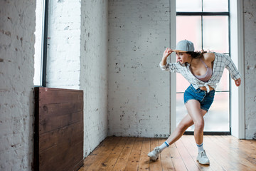 young woman touching cap and dancing hip-hop