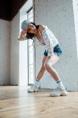 attractive dancer touching cap while dancing hip-hop