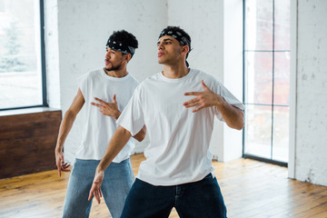 Obraz premium handsome multicultural dancers in headbands gesturing and posing while dancing hip-hop