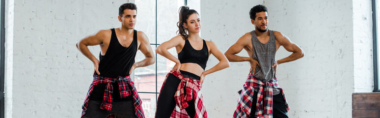 panoramic shot of multicultural dancers with hands on hips dancing jazz funk