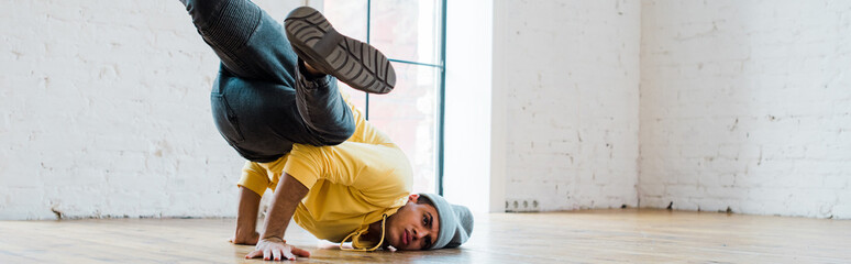 panoramic shot of stylish man in hat breakdancing in dance studio