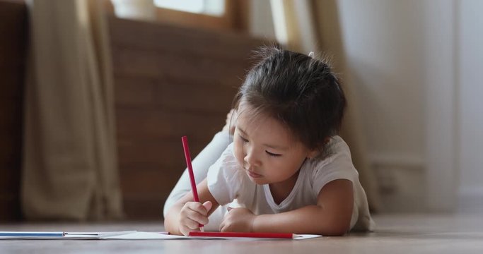 Cute small vietnamese kid girl drawing alone lying on floor