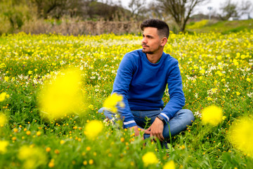 Joven sentado en medio de un campo de flores amarillas mira hacia el lado. bokeh amarillo