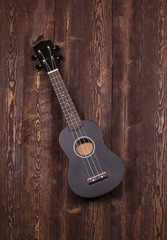 Naklejka premium Ukulele black top view on a wooden background. Classic ukuleles, great design for any purpose.