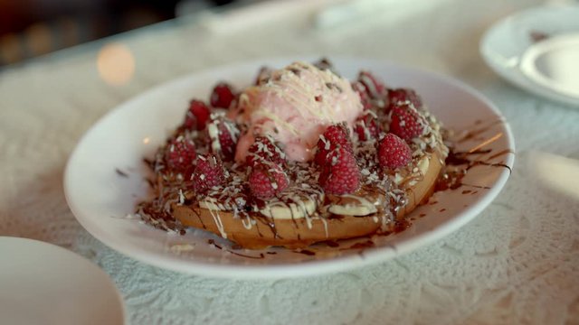 The waiter puts on the table chocolate waffles with raspberries and ice cream