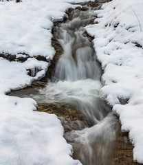 Langzeitbelichtung eines kleinen Baches mit viel frischen Neuschnee