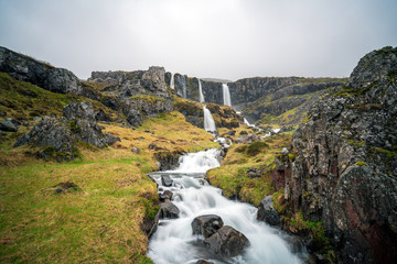 A waterfall cascade in Mjoifjordur in East Iceland near Klifbrekkufossar. Foggy and rainy weather. Longe exposure shot. Landscape, scenery and traveling concept.