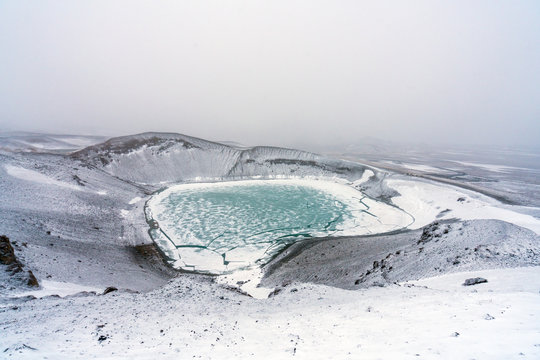Ovelooking ice covered Viti volcanic crater near Krafla geothermal area in Iceland. Foggy and snow covered landscape with frozen green lake at the bottom. Volcano, energy and weather concept.