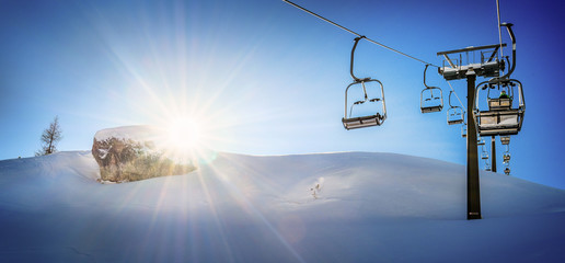 Panorama of ski lift and empty seats in the air on steel ropes at sunny winter day.