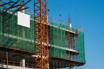 Crane and building construction site against blue sky. Metal construction of unfinished building on construction. Tower Crane use for building of multi storage building.