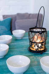 Morning tea party. White bowls and lamp with a candle on a wooden turquoise table. Vertical