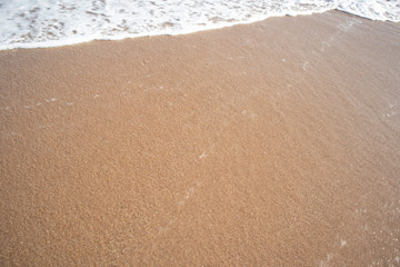 The red sandy beach is covered with white wave bubbles above in the evening.