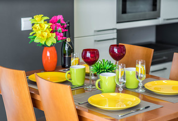 Wooden table. Yellow plates. Mugs. Water in glasses. Wine glasses. Bottle of champagne.