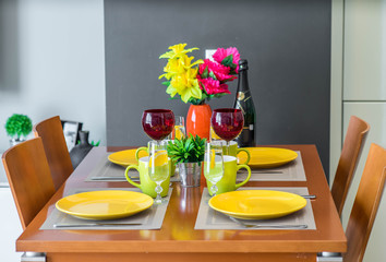 Wooden table. Yellow plates. Mugs. Water in glasses. Wine glasses. Bottle of champagne.