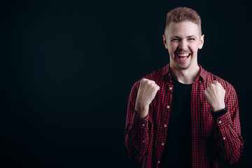 Young handsome man shows success emotions with his fists clenched isolated black background copyspace