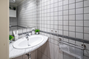 Interior of bathroom with grey tile on the walls. Sink with mirror. Green flowers.