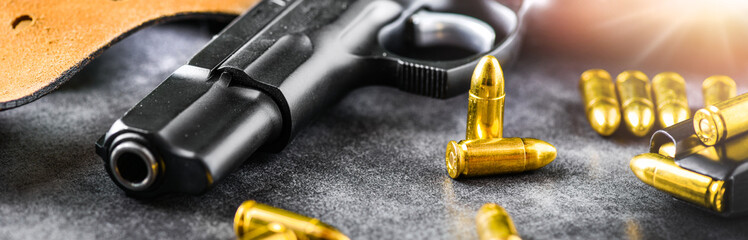 Detail of 9mm pistol, bullets and handcuffs. Gun with ammunition on dark stone background. Banner or panorama military concept.