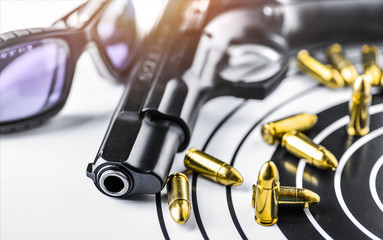 Hand gun detail with ammunition on paper target. 9 mm pistol gun weapon and bullets at dark background.