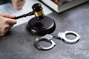 Judge Hand Striking Gavel With Handcuffs On Desk
